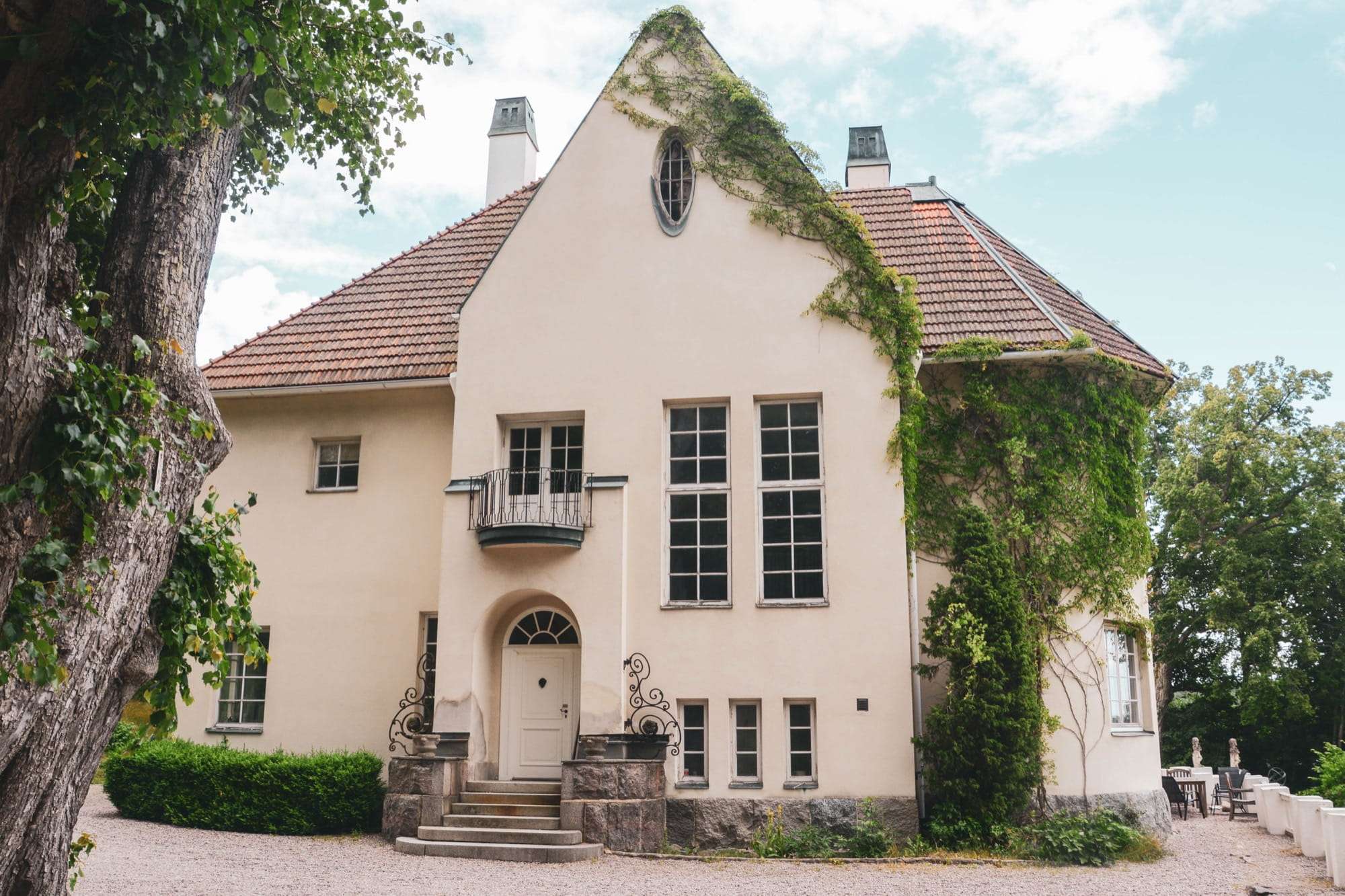 Entrésidan med gavel, rundfönster, valvad ytterdörr, granittrappa och vildvin över hörnet.